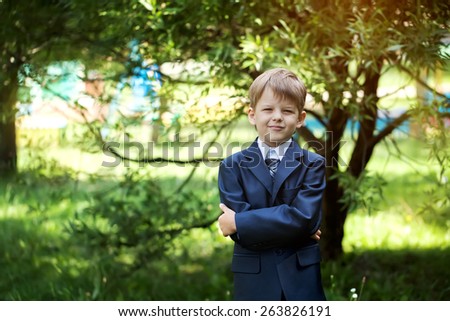male elementary school student with backpack on green background, outdoors
