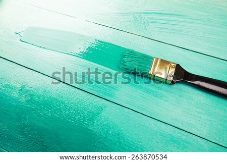 Varnishing a wooden shelf using paintbrush, turquoise color
