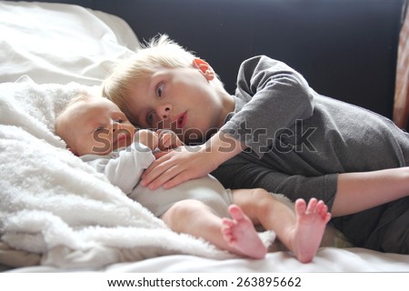 A big brother is lovingly hugging his newborn baby sister as they lay in bed together. Royalty-Free Stock Photo #263895662