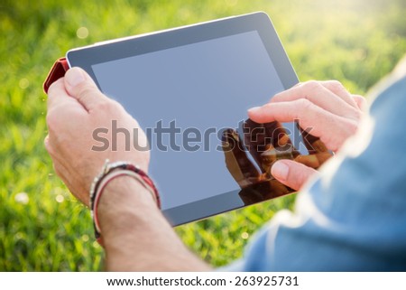 Adult man relaxing at the park with a digital tablet. Lens flare on the upper side of the image. Clipping path of the touch screen included. 