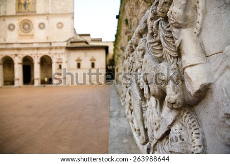 A roman high relief sculpture in the cathedral square of Spoleto with the cathedral's facade in the background, Italy