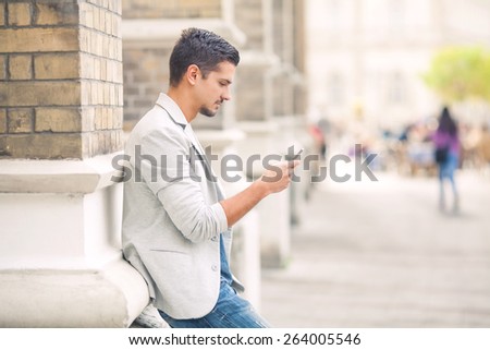 Attractive young man using mobile phone while relaxing in the city