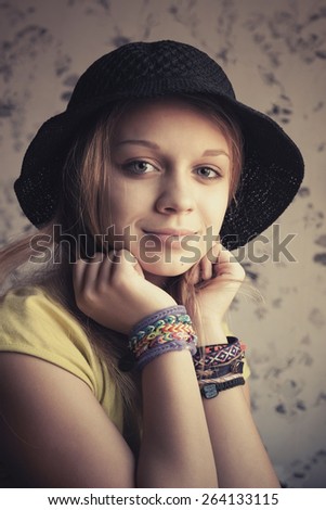 Retro stylized portrait of beautiful blond teenage girl in black hat and rubber loom bracelets. Vintage toned photo filter, instagram style effect