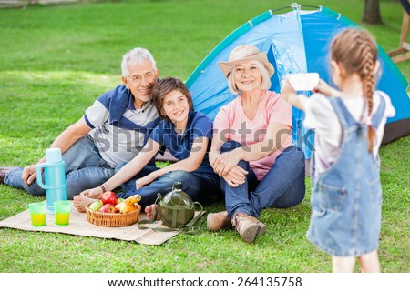Girl photographing family through smartphone at campsite
