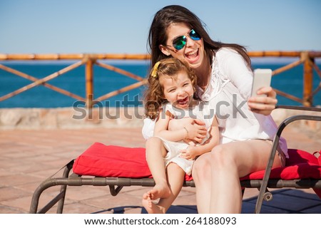 Little girl and her mom having some fun at the beach and taking a selfie with a smartphone