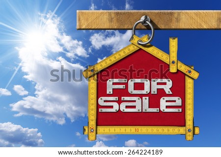 House For Sale Sign - Wooden Meter. Yellow wooden meter ruler in the shape of house with text for sale. For sale real estate sign on blue sky with cloud and sun rays