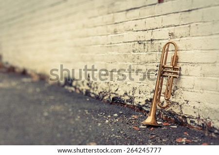 Old worn trumpet stands alone against a grungy pealing white brick wall outside a jazz club Royalty-Free Stock Photo #264245777