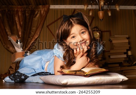 Little girl in blue dress lying on the floor in a room reading a book