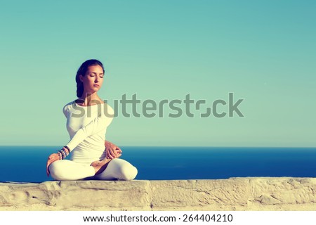 Front portrait of gorgeous young woman practicing yoga on a sunny day with amazing sea horizon on background, woman seeking enlightenment through meditation,relaxed girl performing yoga routine,filter Royalty-Free Stock Photo #264404210