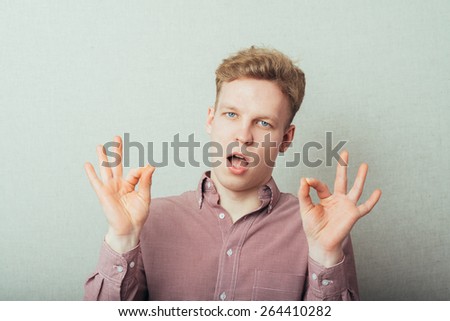 Gesturing OK sign. Cheerful young man in shirt and tie gesturing OK sign while standing against grey background