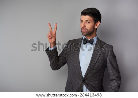Portrait of elegant casual young man wearing tweed jacket and bow tie. Man showing victory sign and looking at camera