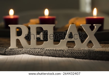 Text of the words relax with burning candles in the background. Relaxation concept for a spa or health retreat Royalty-Free Stock Photo #264432407
