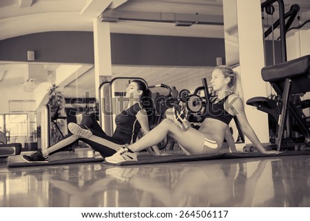 Two beautiful young fit woman stretching legs in the gym