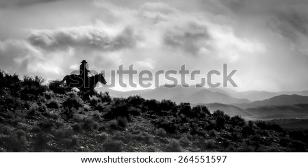 One Silhouetted Cowboy on a Horse in black and white - Silhouette of a cowboy and horse riding down a ridge with the dramatic sky above and the ranges/valleys below