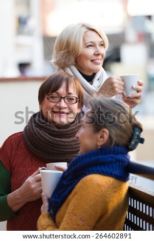 Group of positive senior women drinking tea at balcony. Focus on brunette