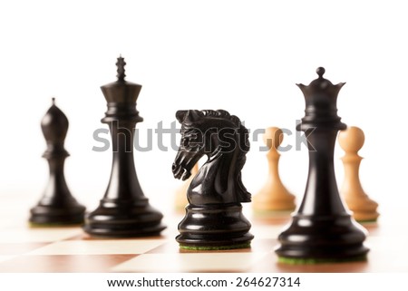 Black chess pieces with white pawns in the background on a chessboard