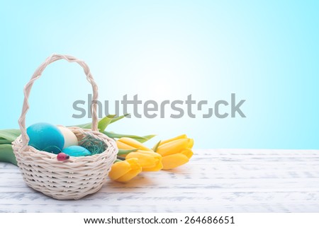 Beautiful Easter eggs in a basket. Delicate yellow spring tulips. Spring Easter holidays. Wooden board rustic