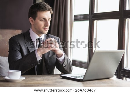 Handsome young businessman working at laptop with cup of coffee in restaurant.