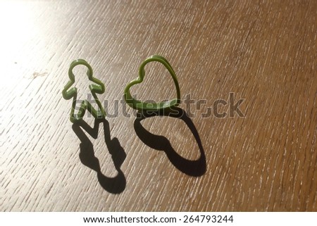 simple single standing man and heart love shaped cutter kept next to each other on a wooden table with shadow extending from it due to sun