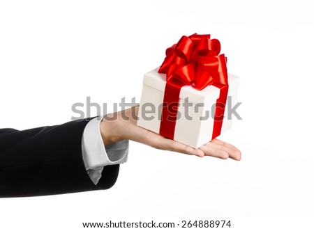 The theme of celebrations and gifts: a man in a black suit holding a exclusive gift wrapped in white box with red ribbon and bow, the most beautiful gift isolated on white background in studio