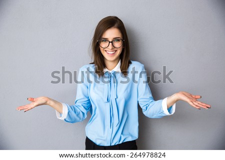 Smiling businesswoman in gesture of asking over gray background. Looking at camera. Wearing in blue shirt and glasses Royalty-Free Stock Photo #264978824