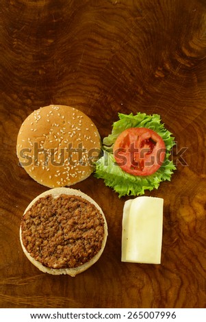 traditional cheeseburger with green lettuce and tomatoes on wooden background top view