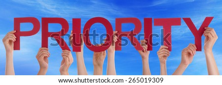 Many Caucasian People And Hands Holding Red Straight Letters Or Characters Building The English Word Priority On Blue Sky