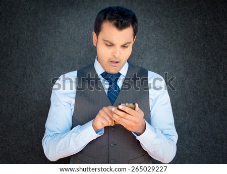 Closeup portrait, funny young man in vest and blue tie, shocked surprised, wide open mouth, by what he sees on his cell phone, isolated gray black background.