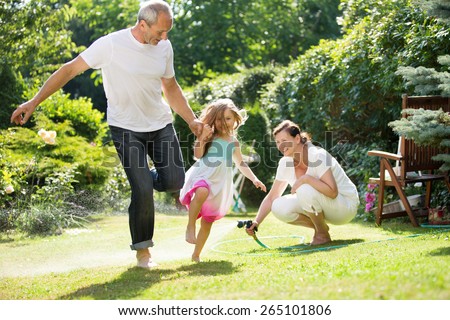 Girl and grandparents playing and waterin garden Royalty-Free Stock Photo #265101806