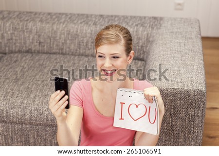 Young woman making selfie, I love you on notepad, smiling
