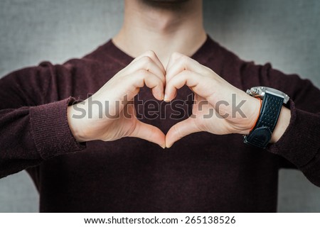 Closeup portrait handsome smiling young business man makes the heart using fingers, hands, isolated grey wall background. Positive human emotions, facial expressions, feelings, body language, attitude Royalty-Free Stock Photo #265138526