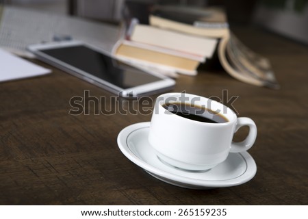 Photo of a no name coffee cup and a stack of books in background on a wood table with shallow depth of field