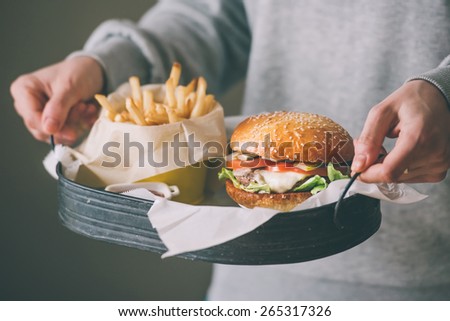 Set of classic american cheese burger and french fries in hands. Toned picture