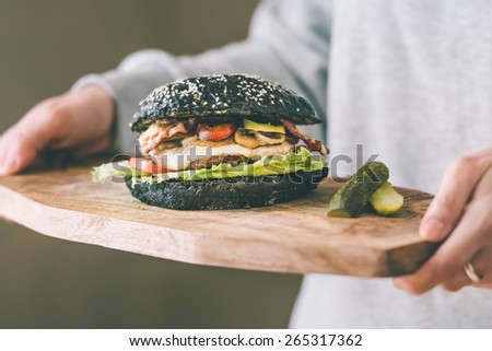 Modern black burger on wooden board in hands. Toned picture