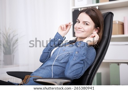 Contented businesswoman sitting listening to music as she relaxes in her office chair during a work break smiling at the camera with pleasure