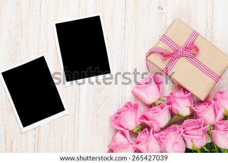 Pink roses and valentines day gift box and two blank photo frames over wooden table. Top view with copy space