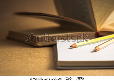 Pencils on notebook with old opened book