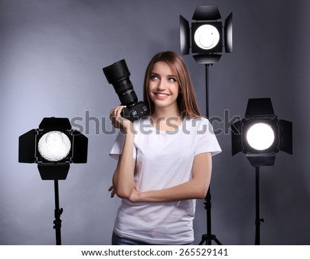 Young female photographer taking photos on grey background