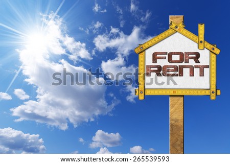 House For Rent Sign - Wooden Meter. Yellow wooden meter ruler in the shape of house with text for rent. For rent real estate sign on blue sky with clouds and sun rays