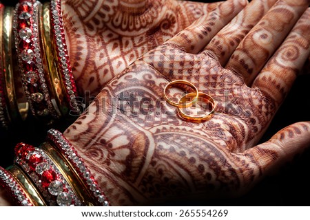 Woman hands with henna holding two golden wedding rings on black background 