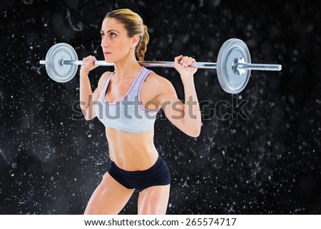 Strong female crossfitter lifting barbell behind head against black background