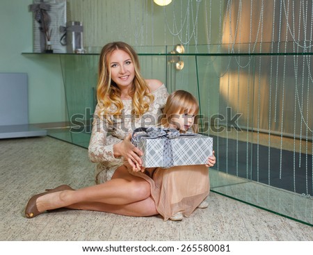Young mother hugging her daughter, holding gift for a holiday home in the interior. The concept of family happiness.