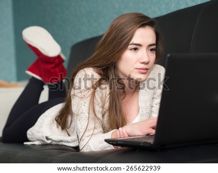 Young girl laying on a sofa and reading from her computer.