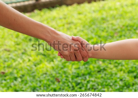 Handshake mother and daughter on grass background