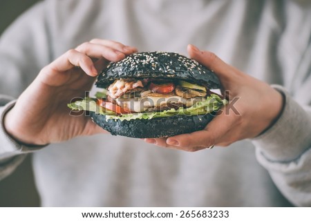 Modern black burger in hands. Toned picture