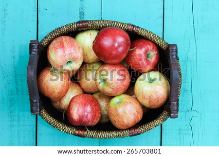 Wicker basket full of red gala apples on antique teal blue wooden background; above view looking down with painted copy space