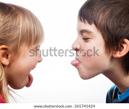 Close-up shot of boy and girl sticking out tongues to each other on white background. Children are half-siblings. Royalty-Free Stock Photo #265741424