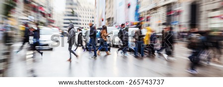picture with zoom effect of a crowd of pedestrians crossing a street in the rainy city