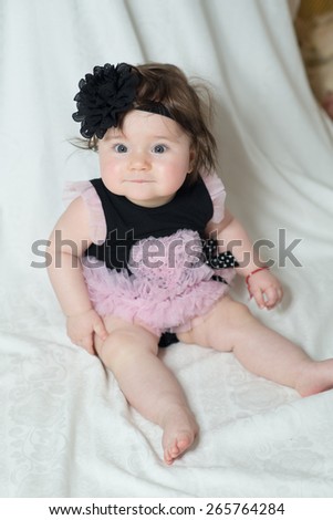 baby in a beautiful dress and a big flower on her head sitting in studio