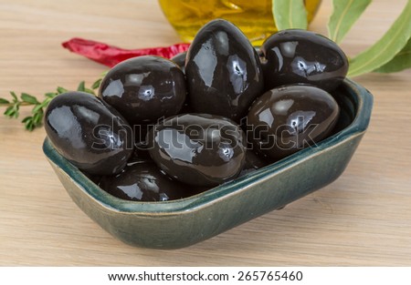 Black olives in the bowl on wood background